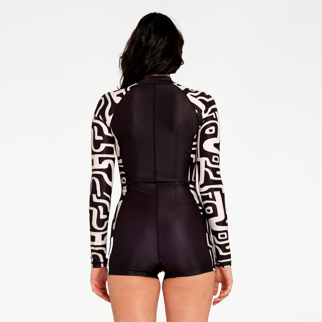 A model shown from the back wearing a long-sleeve one-piece swimsuit with a black and white geometric pattern on the sleeves and a solid black body, set against a plain white background.
