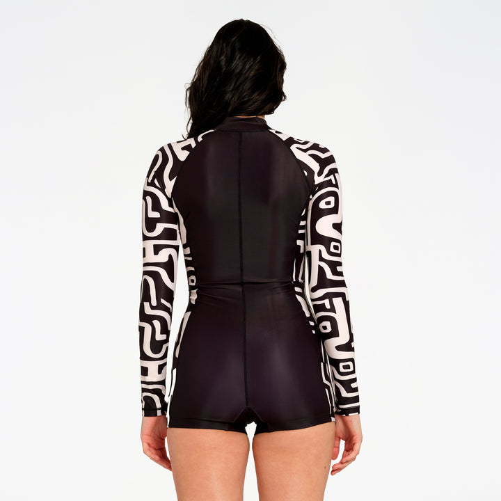 A model shown from the back wearing a long-sleeve one-piece swimsuit with a black and white geometric pattern on the sleeves and a solid black body, set against a plain white background.