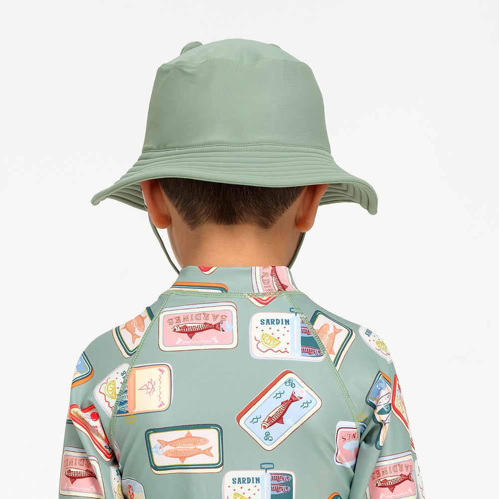 A child shown from the back wearing a sage green sun hat and a matching sage green long-sleeve swimsuit with a colorful fish patchwork print, against a plain white background.