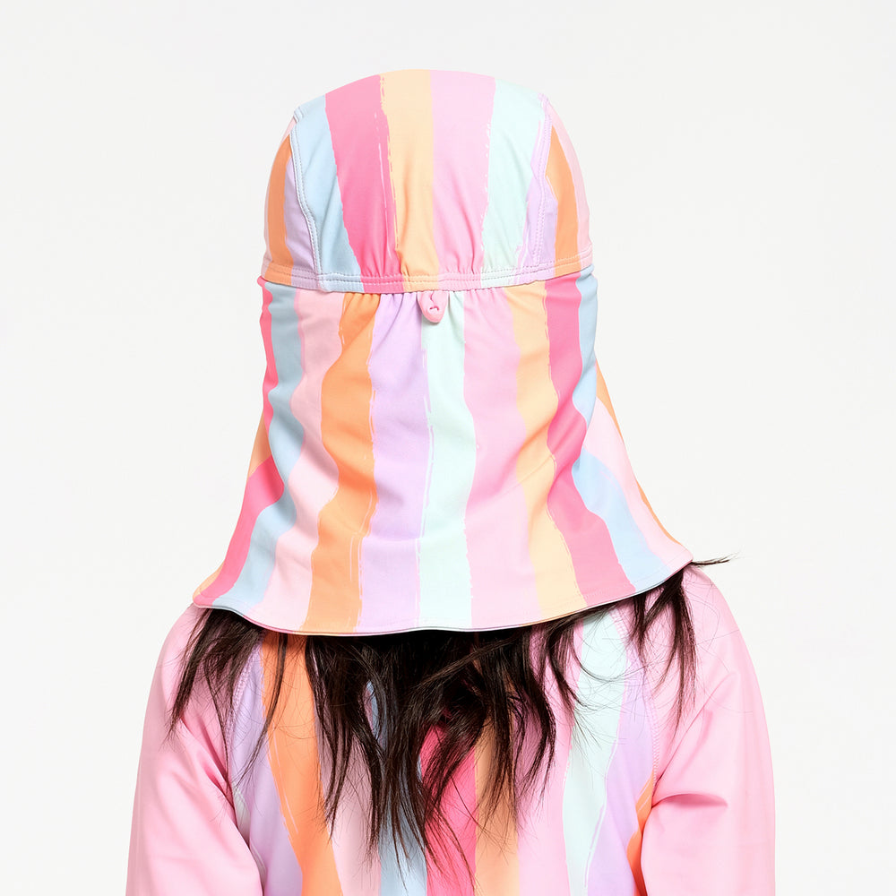 A child viewed from behind wearing a pastel rainbow striped sun hat with an integrated neck flap against a plain white background.