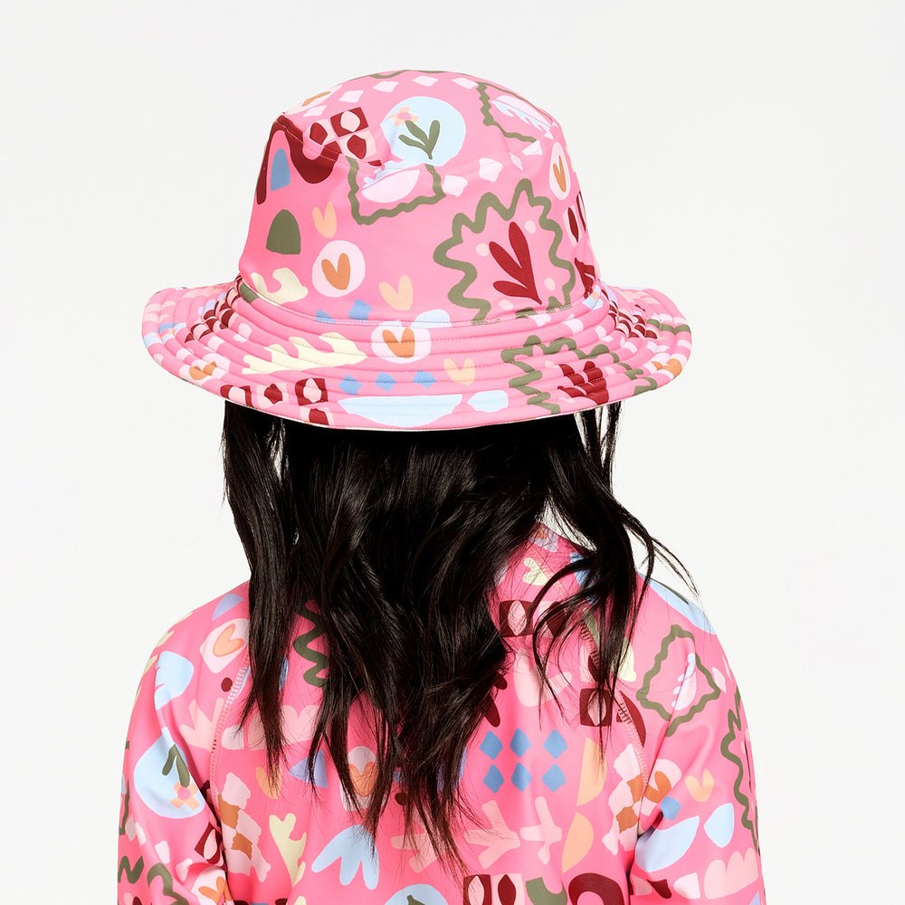 A child shown from the back wearing a pink bucket hat and a matching pink patterned top against a plain white background.