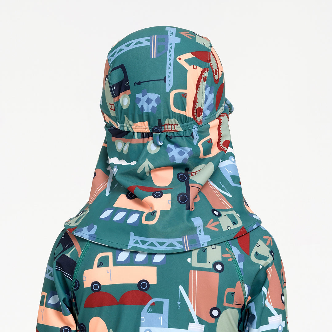 A close-up of a child's swim hat viewed from the back, featuring a teal green base with a playful cartoon construction and vehicle print in orange, blue, beige, and red, set against a plain white background.