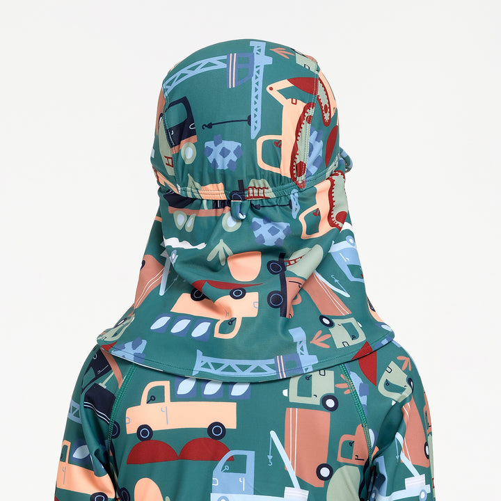 A close-up of a child's swim hat viewed from the back, featuring a teal green base with a playful cartoon construction and vehicle print in orange, blue, beige, and red, set against a plain white background.