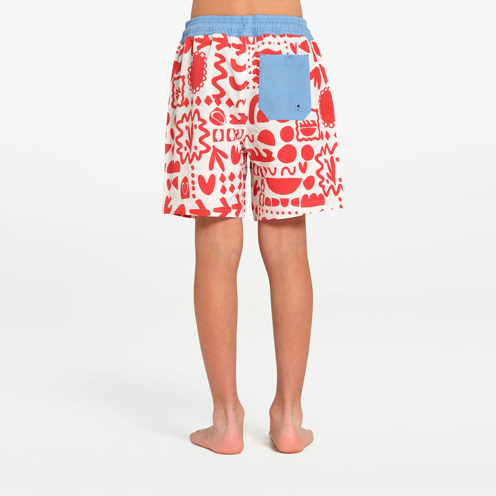 A person shown from the back wearing patterned board shorts with a light blue waistband and pocket, standing barefoot against a plain white studio background.