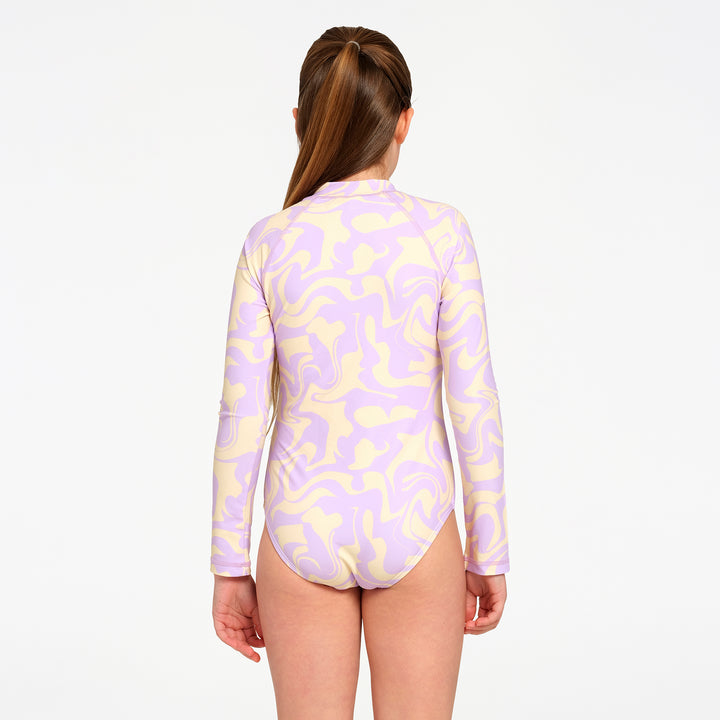 A girl viewed from the back wearing a long-sleeve one-piece swimsuit with a pastel purple and pale yellow abstract wavy pattern, set against a plain white background.