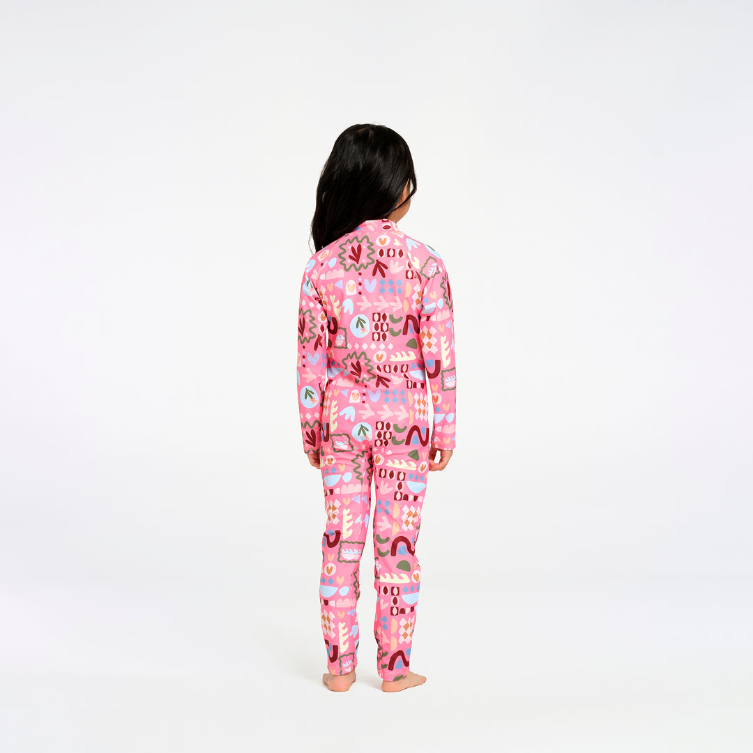 A child standing with their back to the camera, wearing a pink long-sleeve swimsuit with a colorful abstract pattern, photographed against a seamless white background.