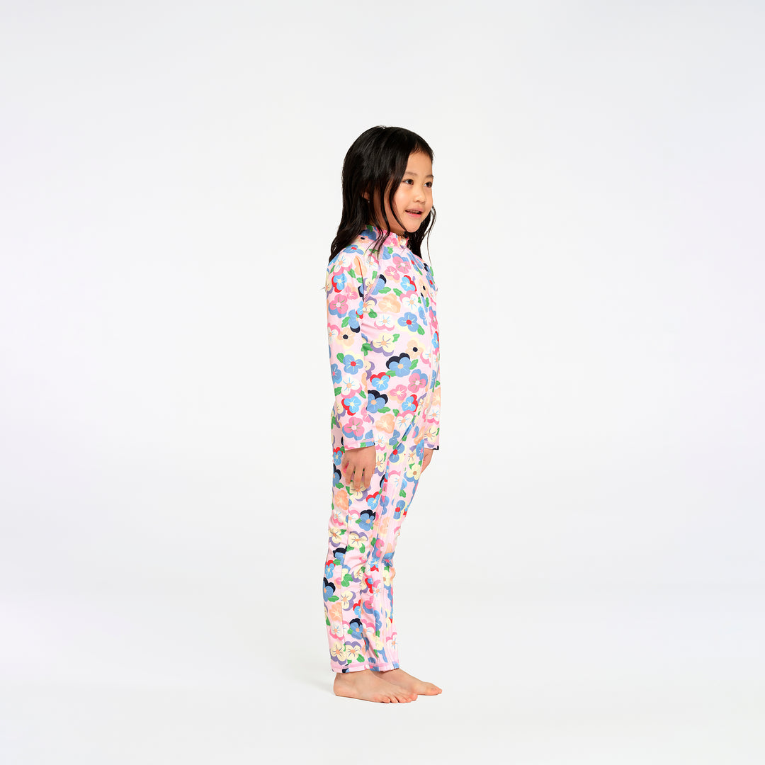 A young girl stands in profile wearing a long-sleeve swimsuit with a colorful floral pattern on a white background.