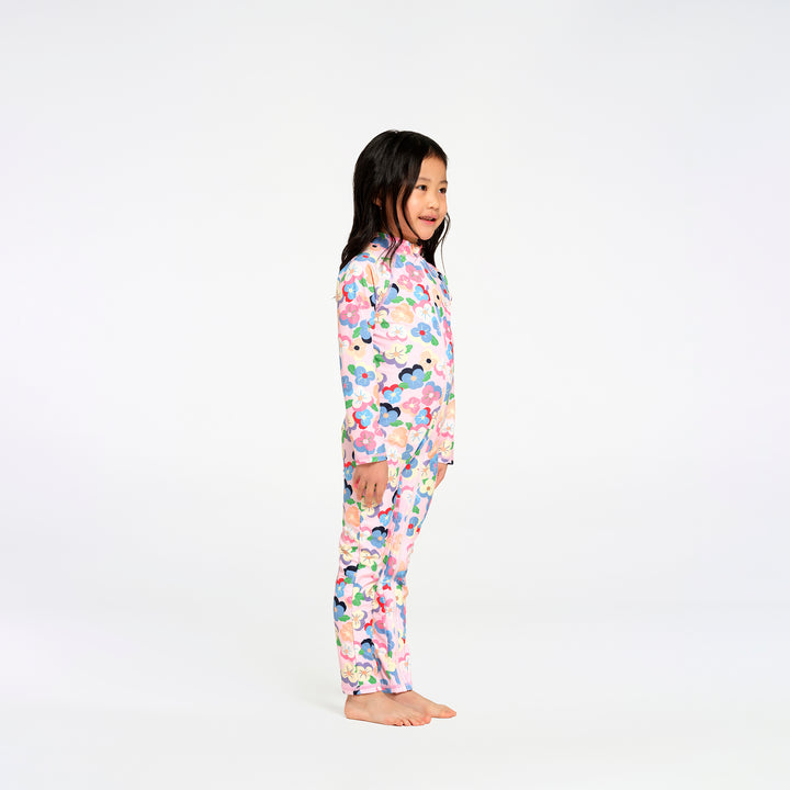 A young girl stands in profile wearing a long-sleeve swimsuit with a colorful floral pattern on a white background.