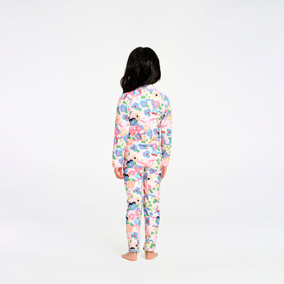 A child standing with their back to the camera, wearing a long-sleeve swimsuit with a colorful floral pattern on a white background.