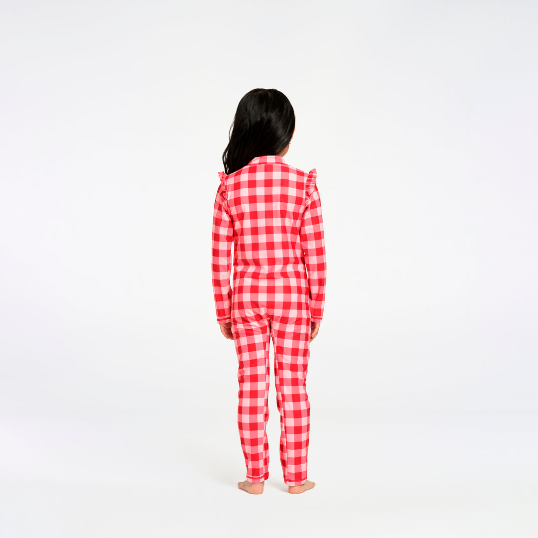 A child standing with their back to the camera, wearing a red and white gingham check long-sleeve swimsuit with ruffled shoulders, against a plain white background.
