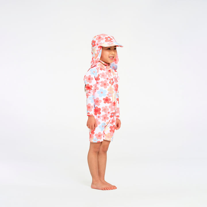 A young child standing in profile wearing a long-sleeve floral swim suit with matching sun hat, on a seamless white studio background.