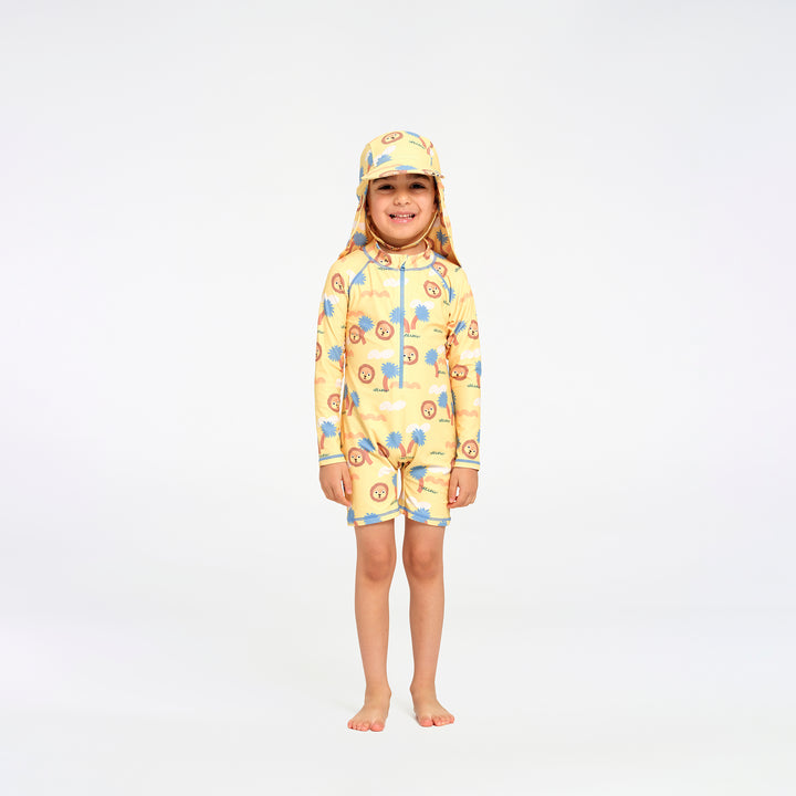 A young child wearing a yellow one-piece swimsuit and matching swim hat with a blue and orange tree pattern, standing against a plain white studio background.