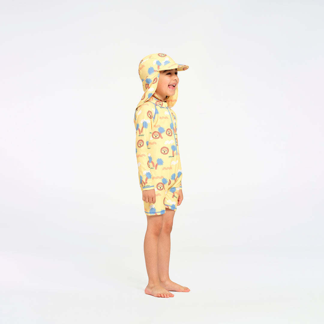 A child wearing a yellow swim suit with a blue and orange jungle pattern and matching hat, standing in profile against a white studio background.