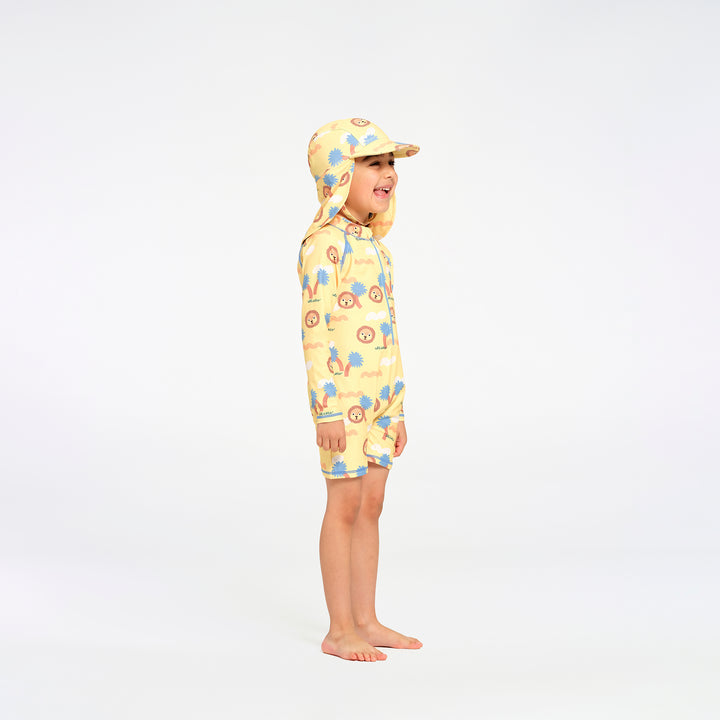 A child wearing a yellow swim suit with a blue and orange jungle pattern and matching hat, standing in profile against a white studio background.