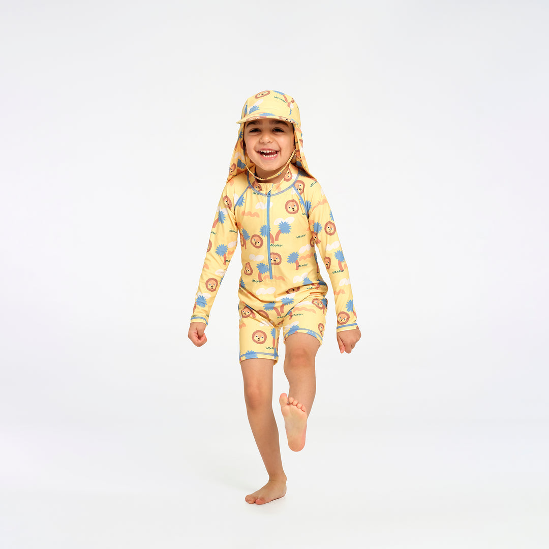 A young child wearing a yellow one-piece swimsuit and matching hat with a blue and orange jungle pattern, running barefoot on a white studio background.