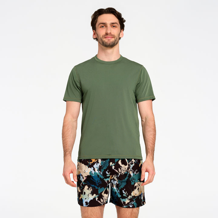 A man modeling a short-sleeve crewneck swim t-shirt in olive green, paired with patterned swim shorts, against a plain white studio background.
