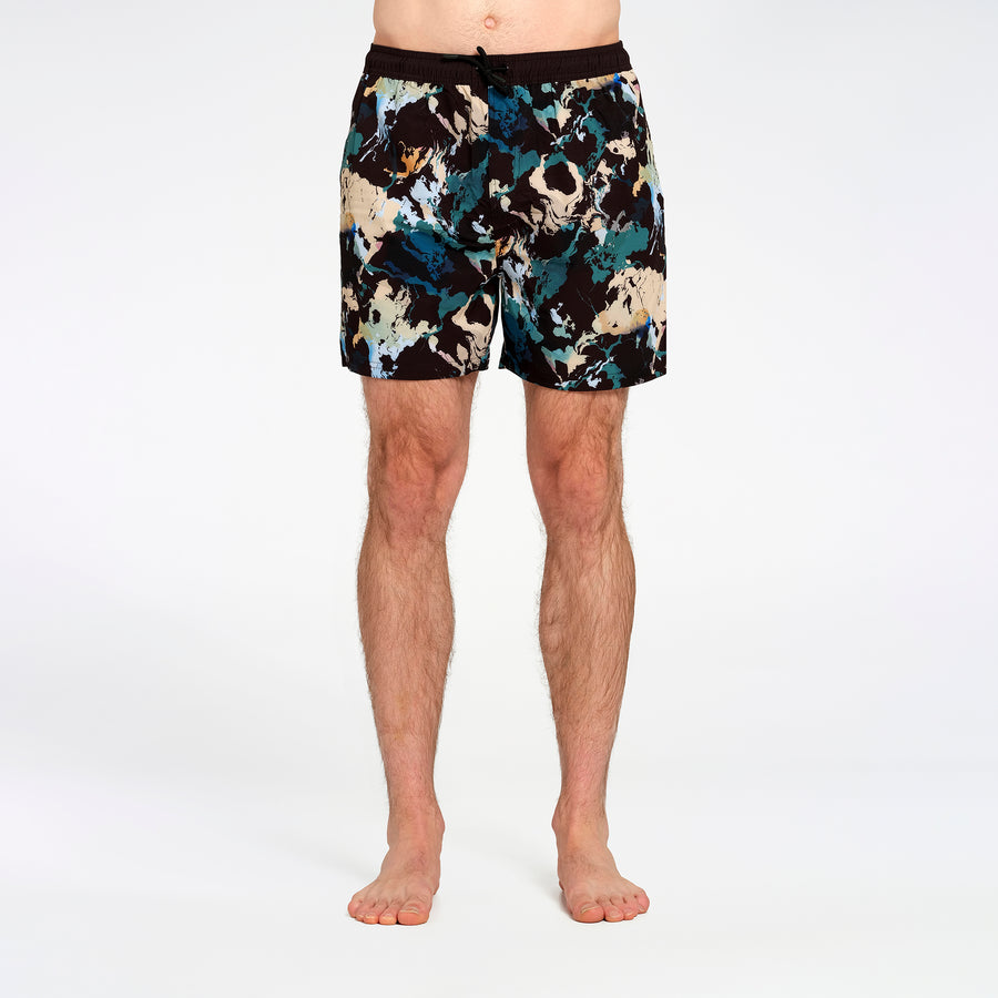 Men's swim shorts with an abstract paint-splatter pattern in black, teal, beige, and white, modeled on a person's lower body against a white studio background.