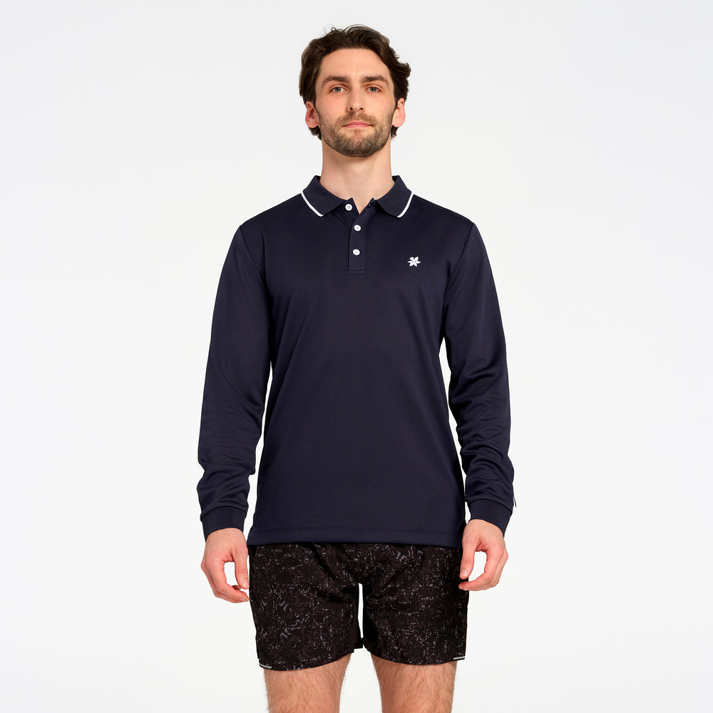 A man wearing a navy blue long-sleeve polo shirt with white trim on the collar and a small white embroidered logo on the chest, paired with black patterned shorts, against a plain white background.