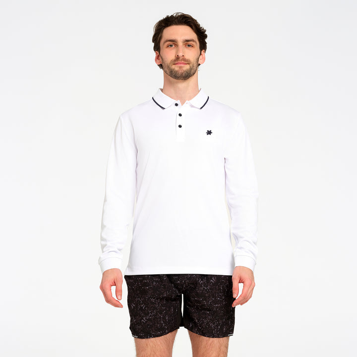 A man modeling a white long-sleeve polo shirt with a black embroidered logo on the left chest, paired with black patterned shorts, against a plain white background.
