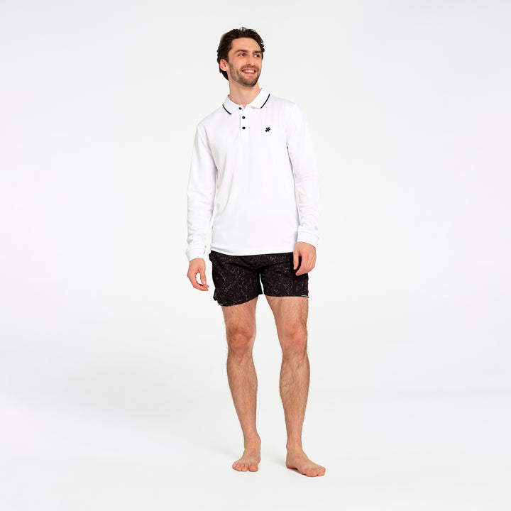 A man modeling a white long-sleeve polo shirt with black trim and black patterned shorts against a plain white studio background.