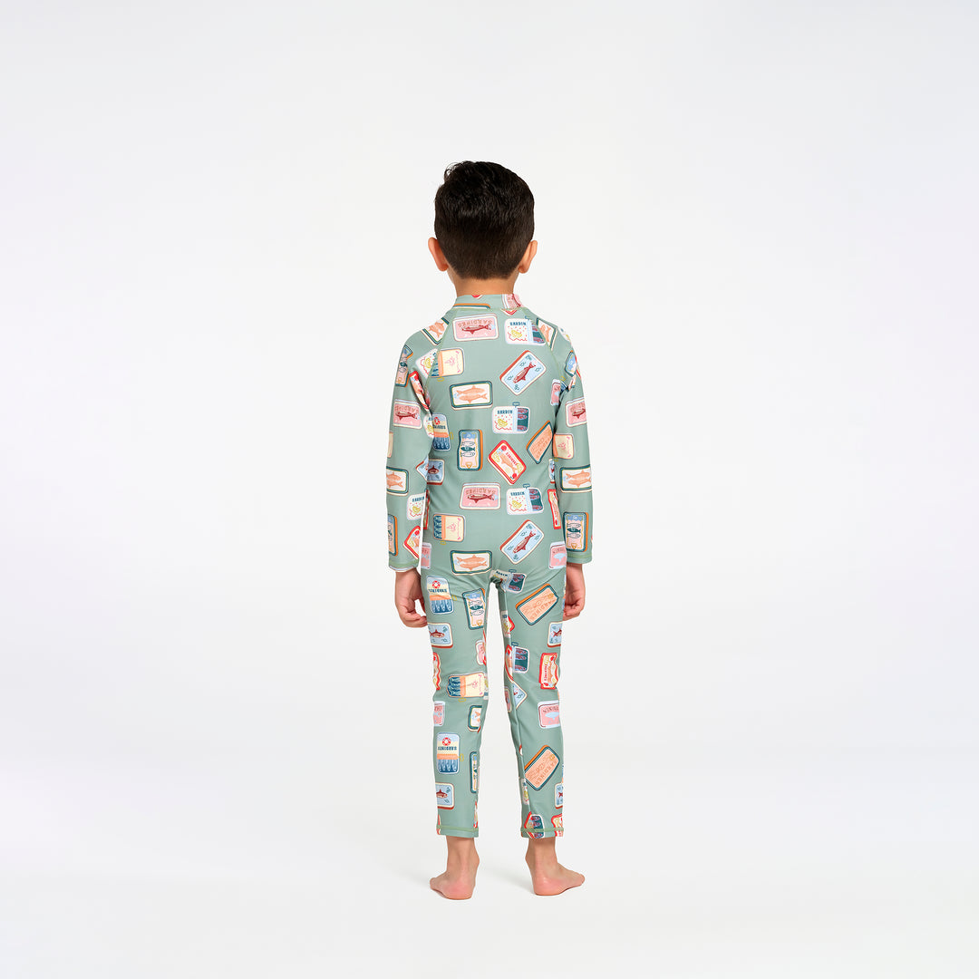 A child standing with their back to the camera, wearing a one piece swim suit in sage green with a colorful retro sardine print, on a seamless white background.