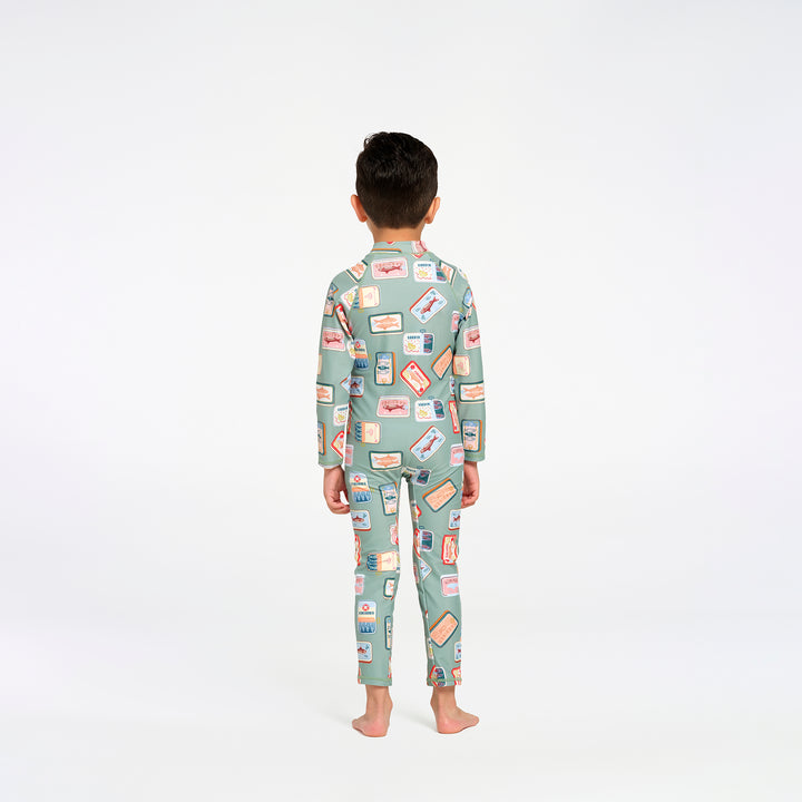 A child standing with their back to the camera, wearing a one piece swim suit in sage green with a colorful retro sardine print, on a seamless white background.