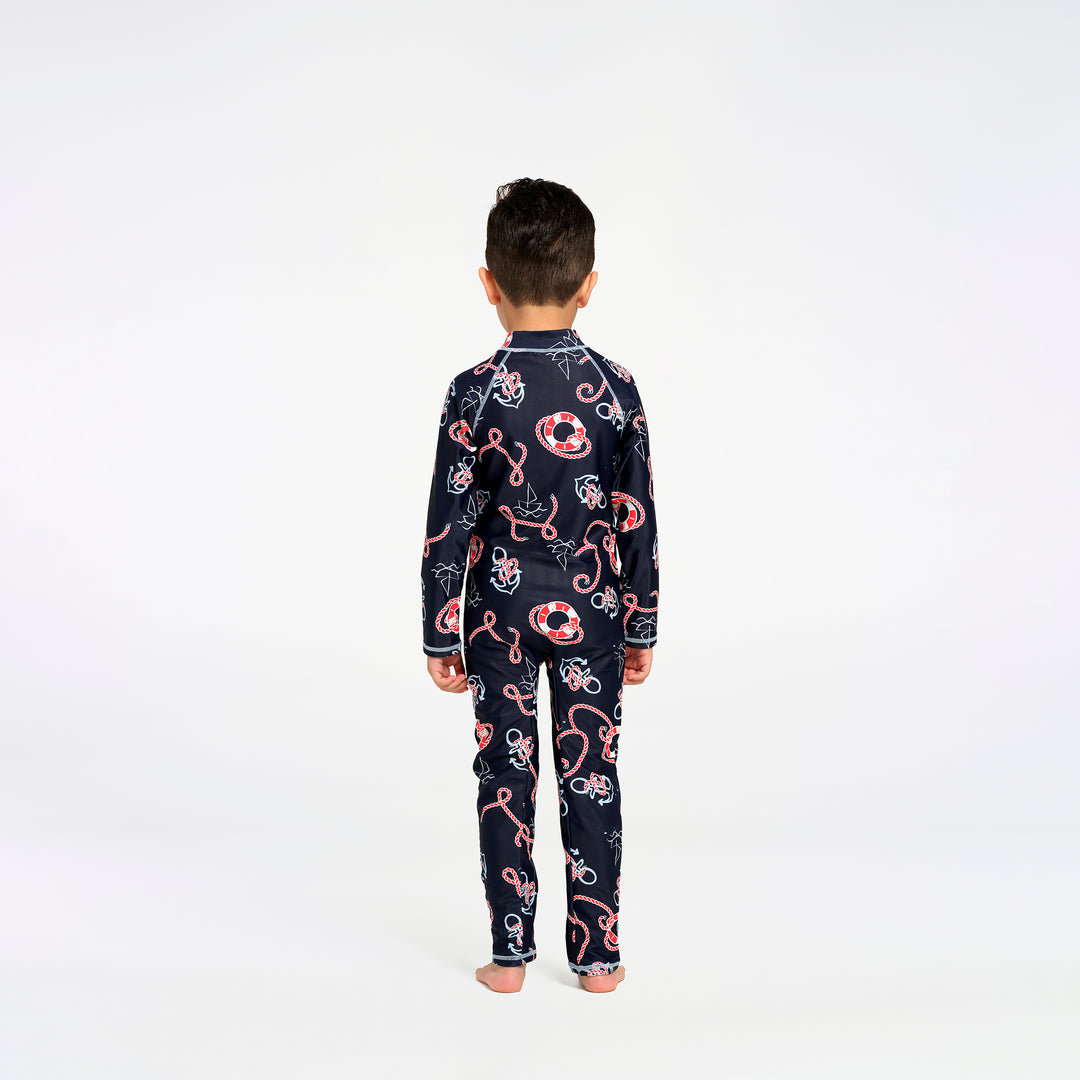 A child viewed from behind wearing a navy long-sleeve swimsuit with a red, white, and light blue nautical pattern, standing against a plain white studio background.