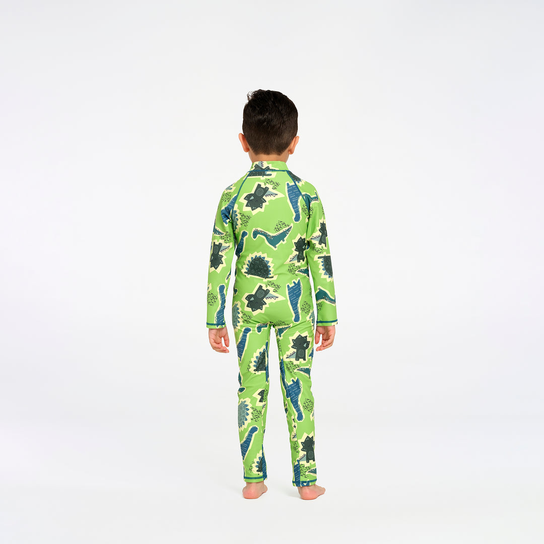 A young boy viewed from behind wearing a green long-sleeve swimsuit with a dinosaur print, standing against a plain white studio background.