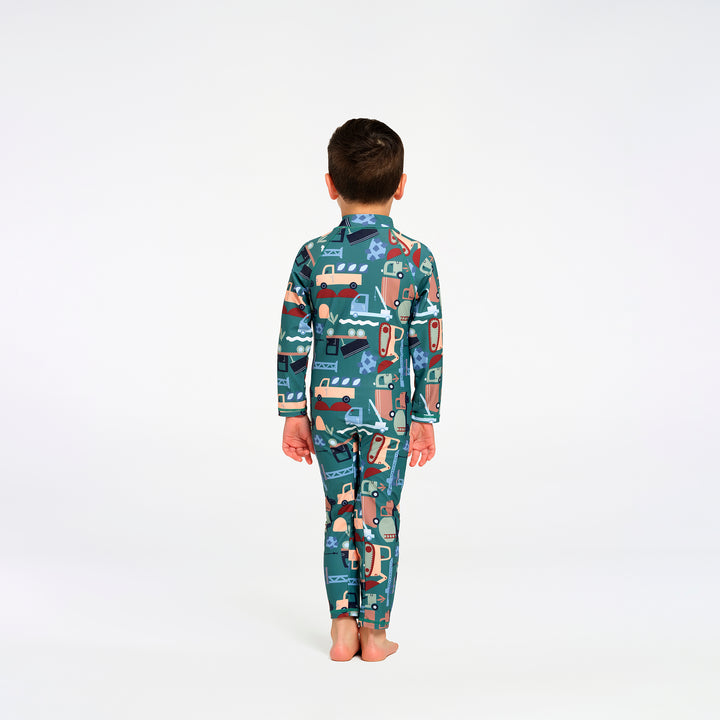 A child standing with their back to the camera, wearing a long-sleeve swimsuit with a colorful cartoon truck pattern on a teal background, set against a plain white studio background.
