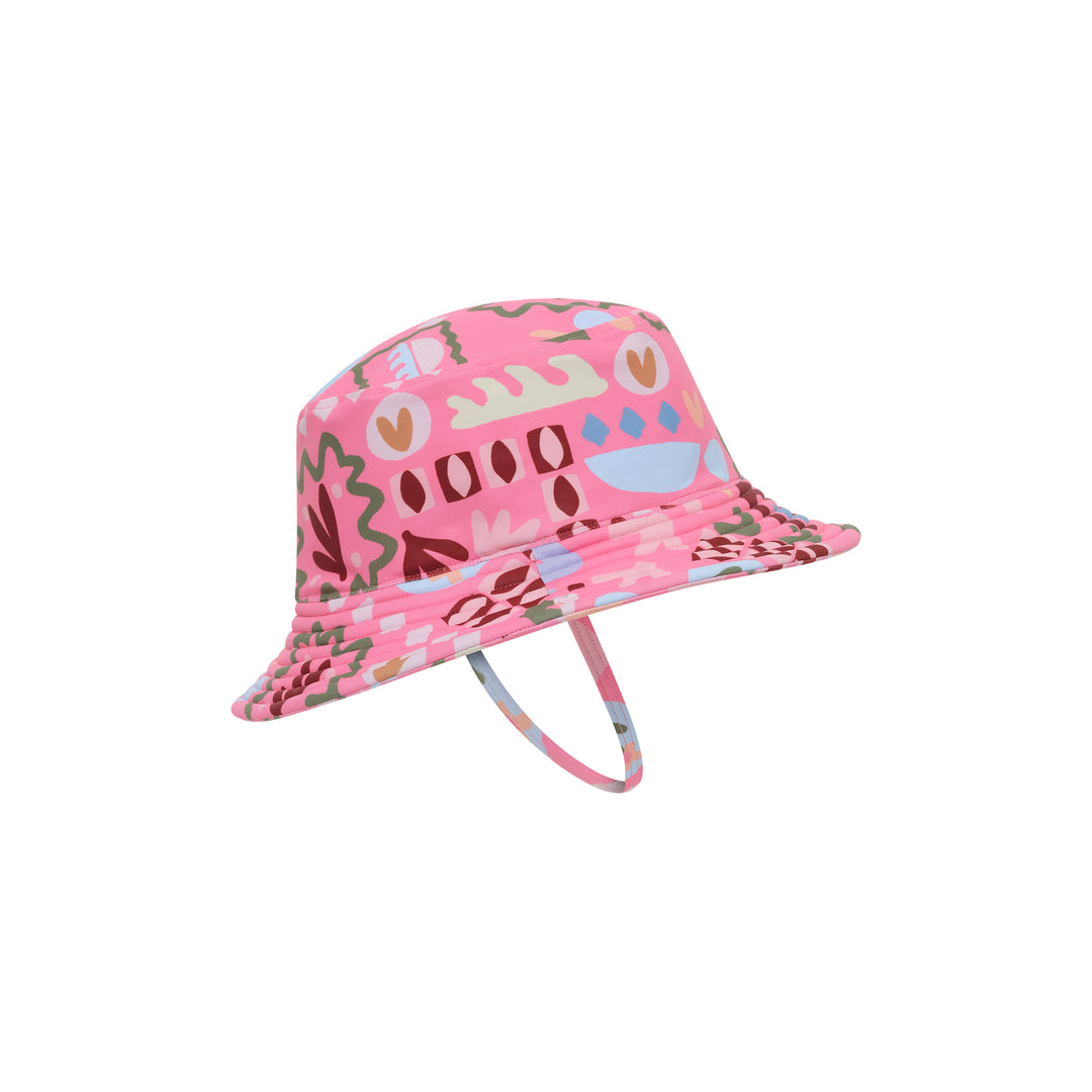 A pink patterned bucket hat with a matching chin strap, featuring a retro abstract design in shades of pink, brown, green, and blue on a solid white background.