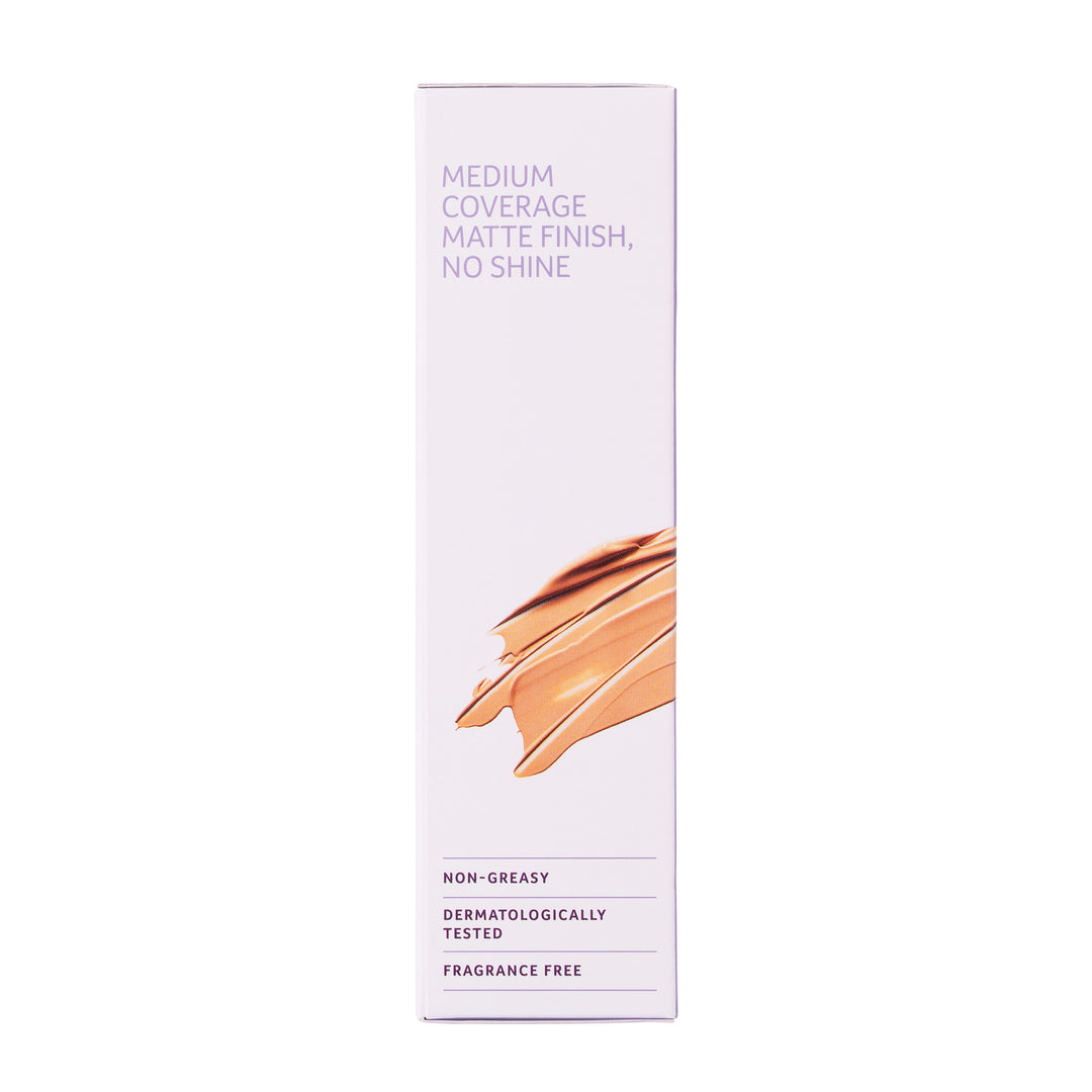 A tall, narrow white sunscreen box with purple text reading 'MEDIUM COVERAGE MATTE FINISH, NO SHINE' and a swatch of warm beige foundation on the front, shown on a plain white background.