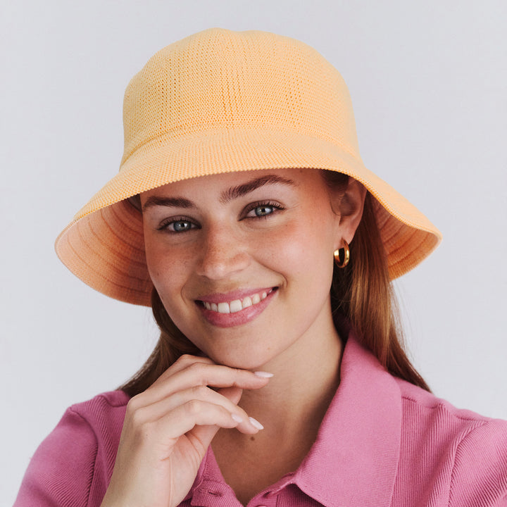 Female model wearing Tamzin Bucket Hat in Apricot colour, front view showcasing fit and wide brim