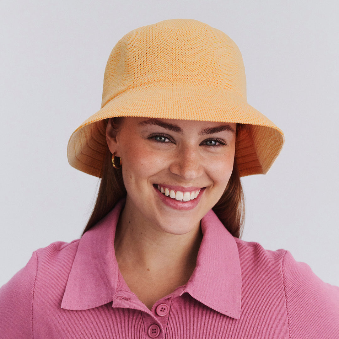 Female model wearing Tamzin Bucket Hat in Apricot colour, three-quarter angle highlighting shape and silhouette