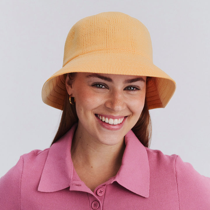 Female model wearing Tamzin Bucket Hat in Apricot colour, three-quarter angle highlighting shape and silhouette