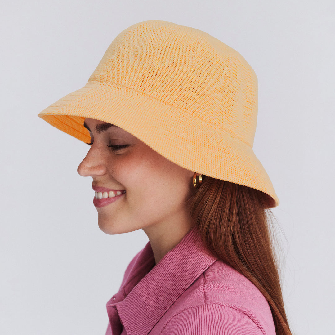 Female model wearing Tamzin Bucket Hat in Apricot colour, side profile showing brim coverage