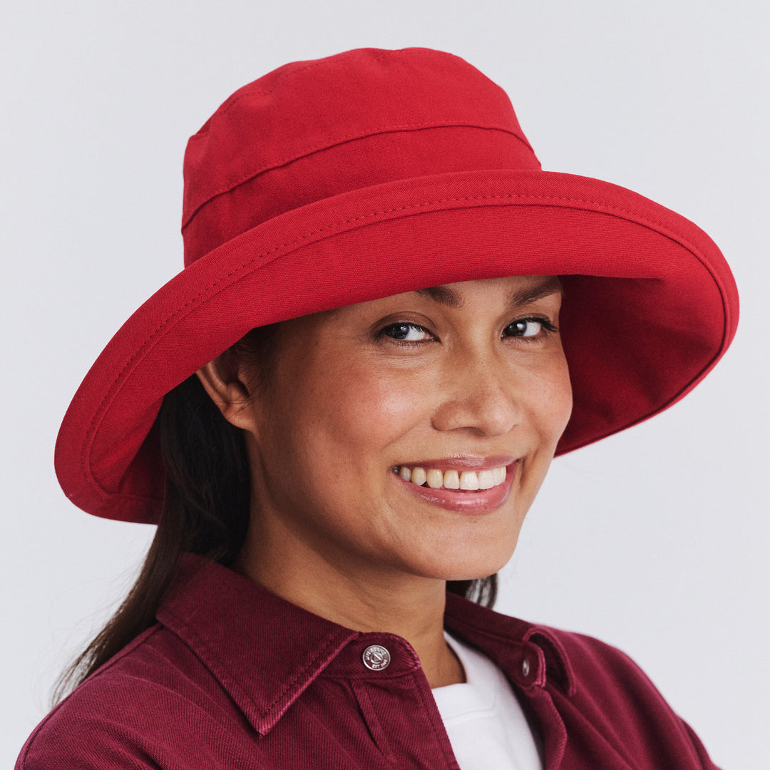 Female model wearing Essential Traveller Hat in poppy red colour, front view styled with red outfit