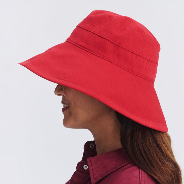 Female model wearing Essential Traveller Hat in poppy red colour, side profile showing brim coverage and silhouette