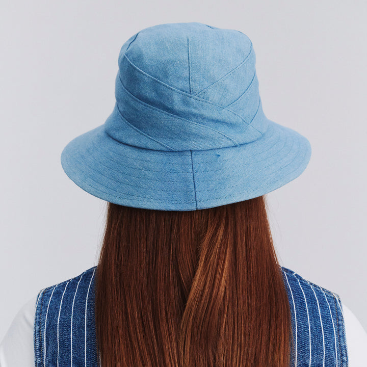 Back view of female model wearing Golf bucket hat in Denim showing brim shape and rear detailing