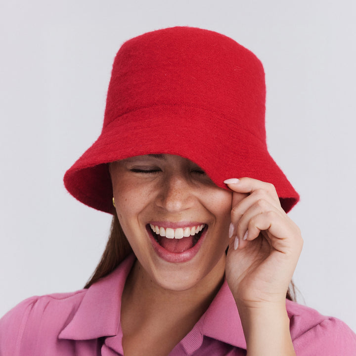 Female model wearing Isadora Bucket Hat in red colour, front view with brim pulled down over eye