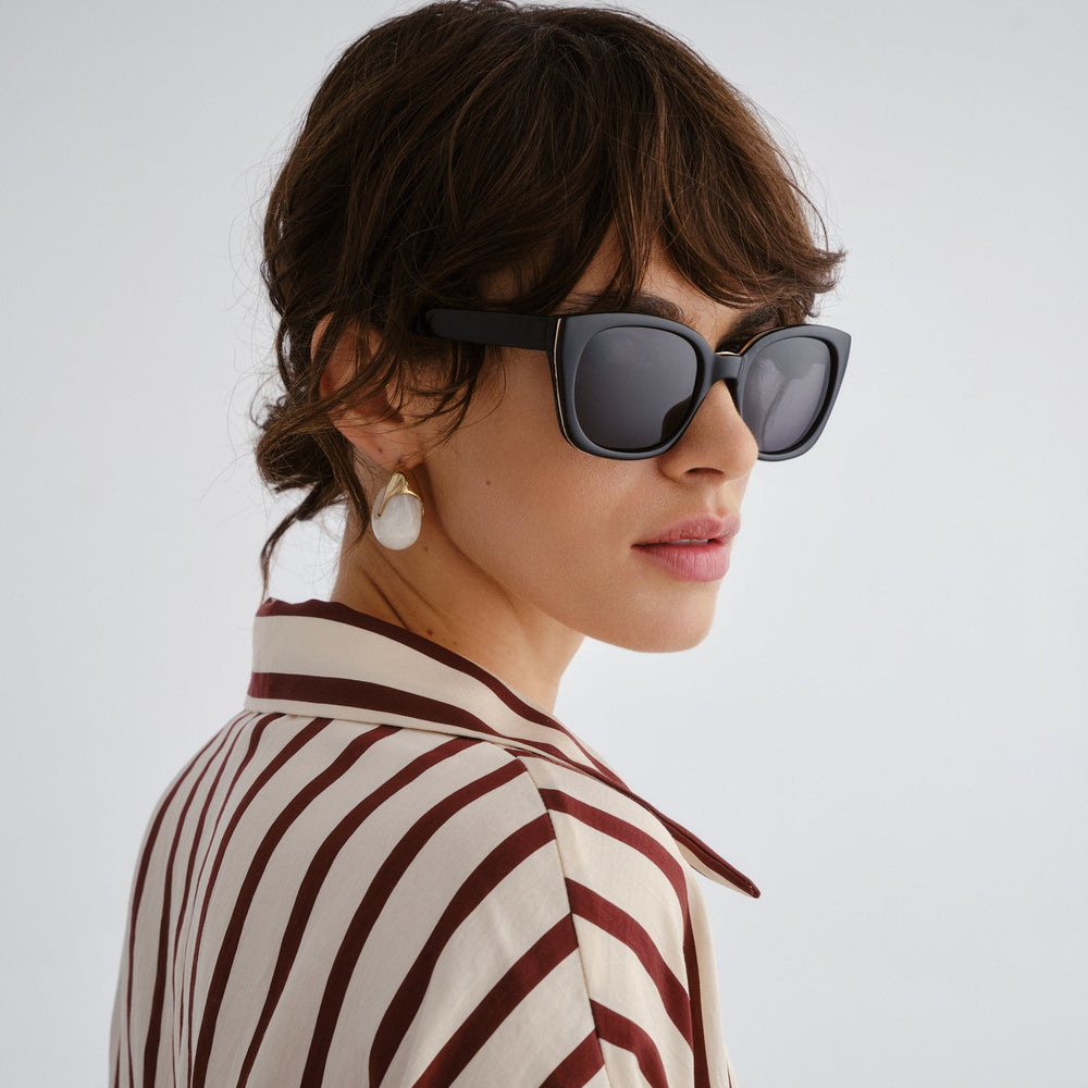 Female model wearing Teneriffe sunglasses in black, side angle highlighting profile and gold temple detail