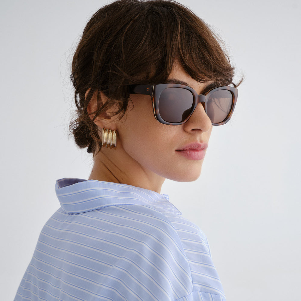 Female model wearing Teneriffe sunglasses in amber tort with gold detailing, side angle highlighting profile and gold temple detail