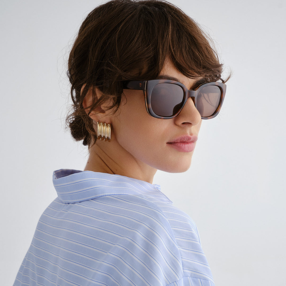 Female model wearing Teneriffe sunglasses in amber tort with gold detailing, side angle highlighting profile and gold temple detail