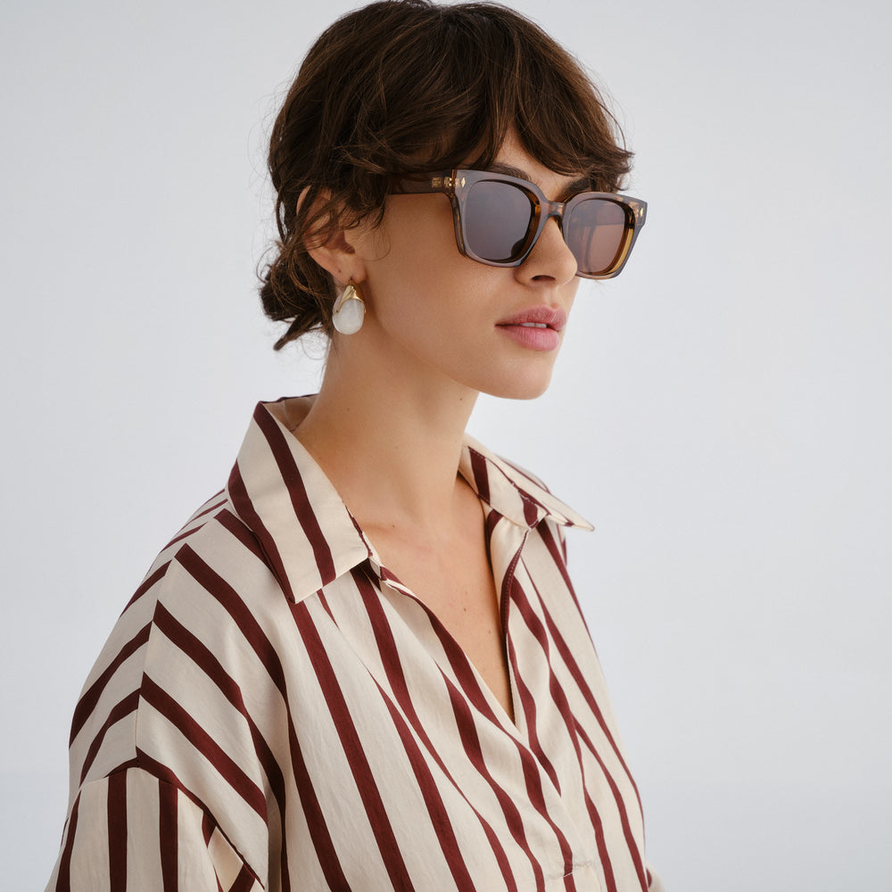 Woman wearing sunglasses and a striped shirt against a plain background
