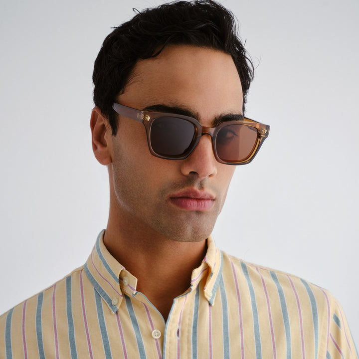 Man wearing sunglasses and a striped shirt against a plain background