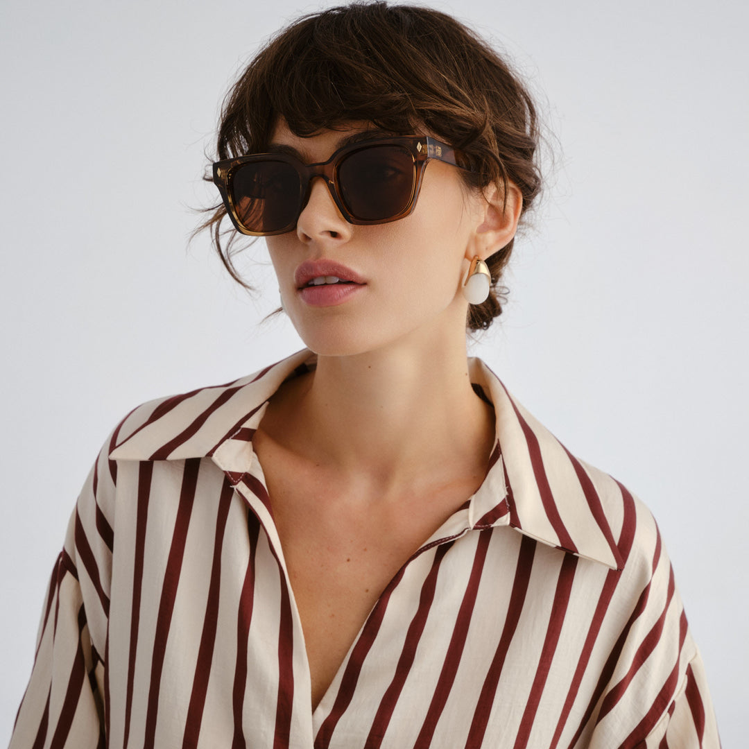 Woman wearing a striped shirt and sunglasses against a plain background