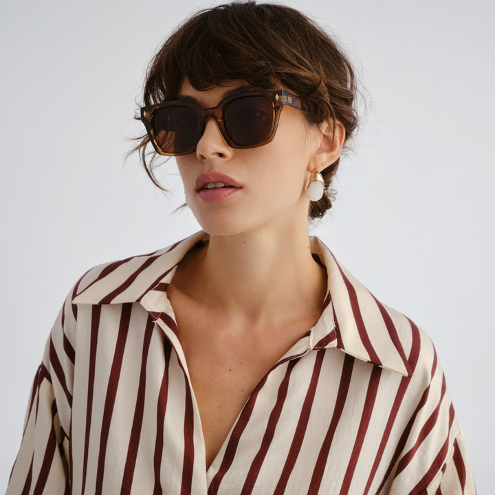 Woman wearing a striped shirt and sunglasses against a plain background