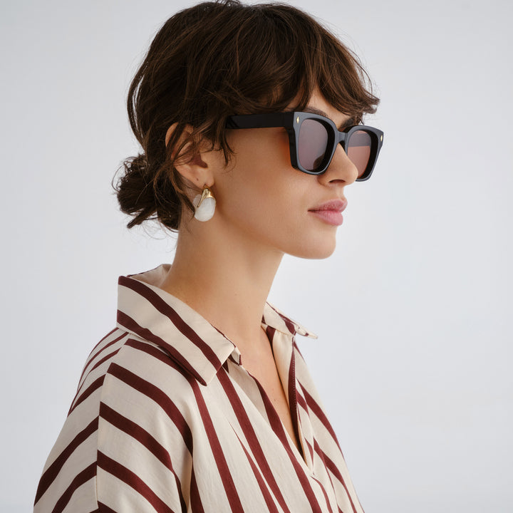 Woman wearing sunglasses and a striped shirt against a plain background, side profile