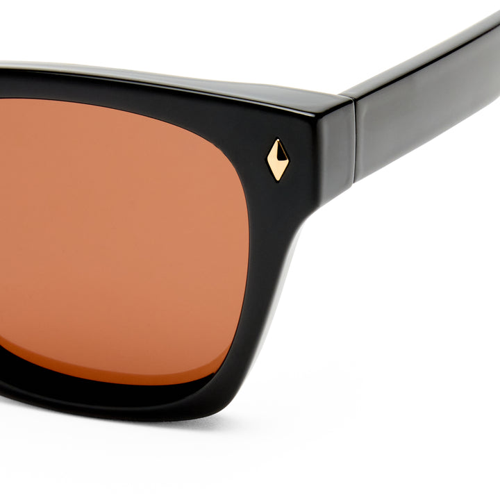 Kingscliff sunglasses with black frame and brown lens on a white background, zoomed on gold detailing