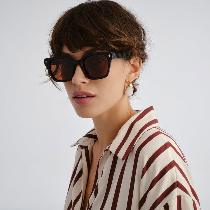 Woman wearing black sunglasses and a striped shirt against a plain background