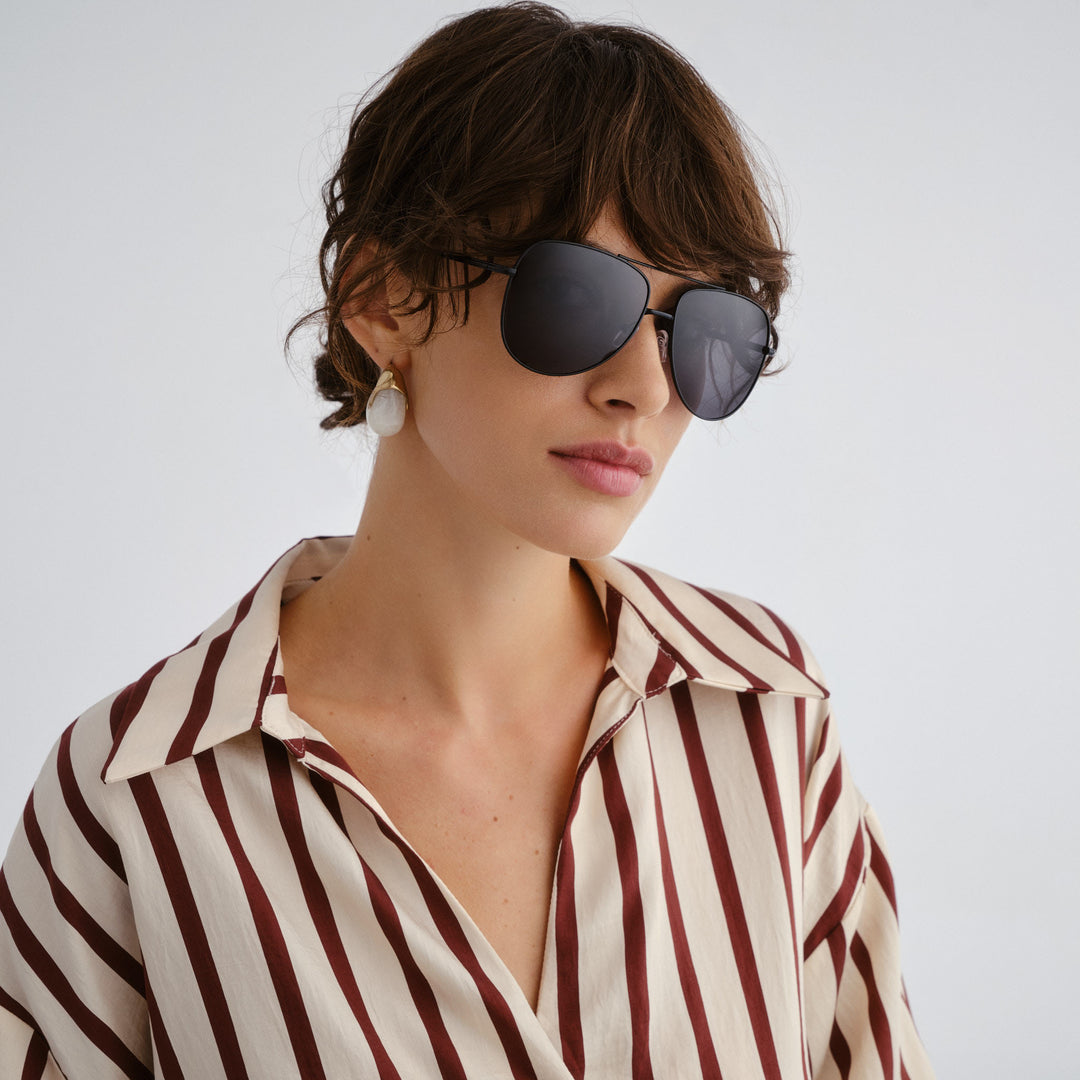 Woman wearing sunglasses and a striped shirt against a plain background